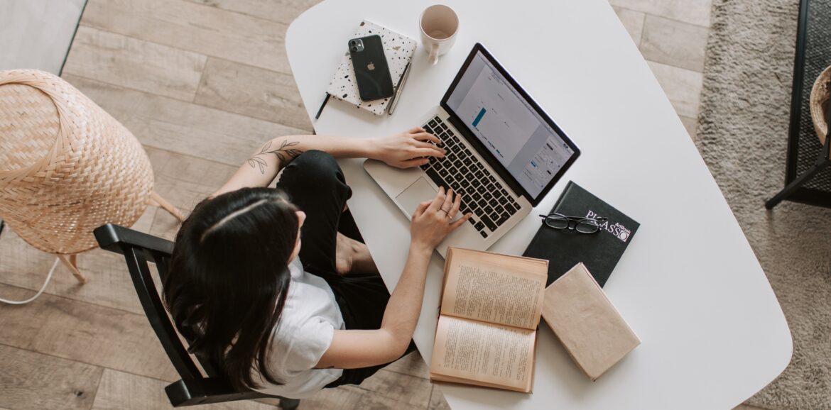 Overhead shot of a woman on a laptop surrounded by books